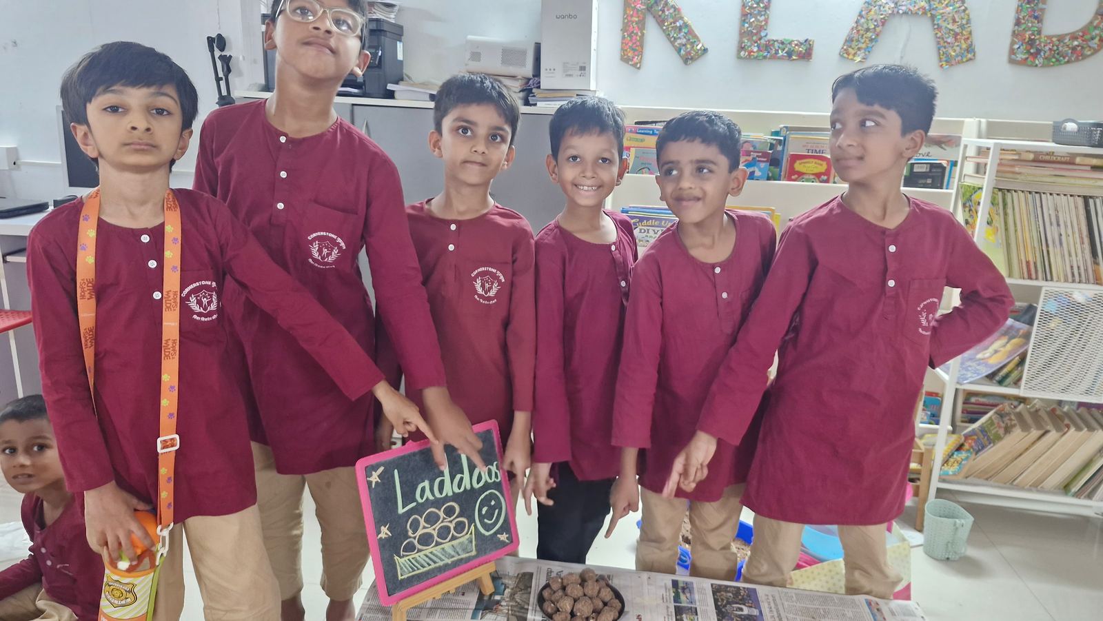 Grade 2 children in maroon kurtas at the laddoo stall they ran
