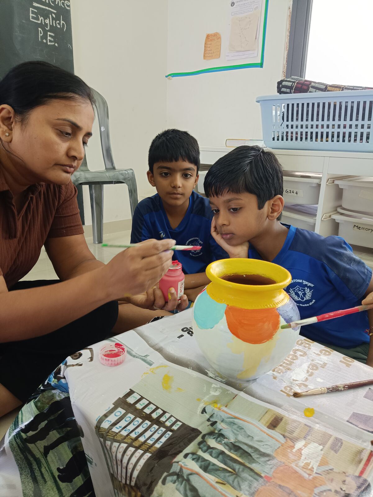 A teacher with two children painting a clay pot