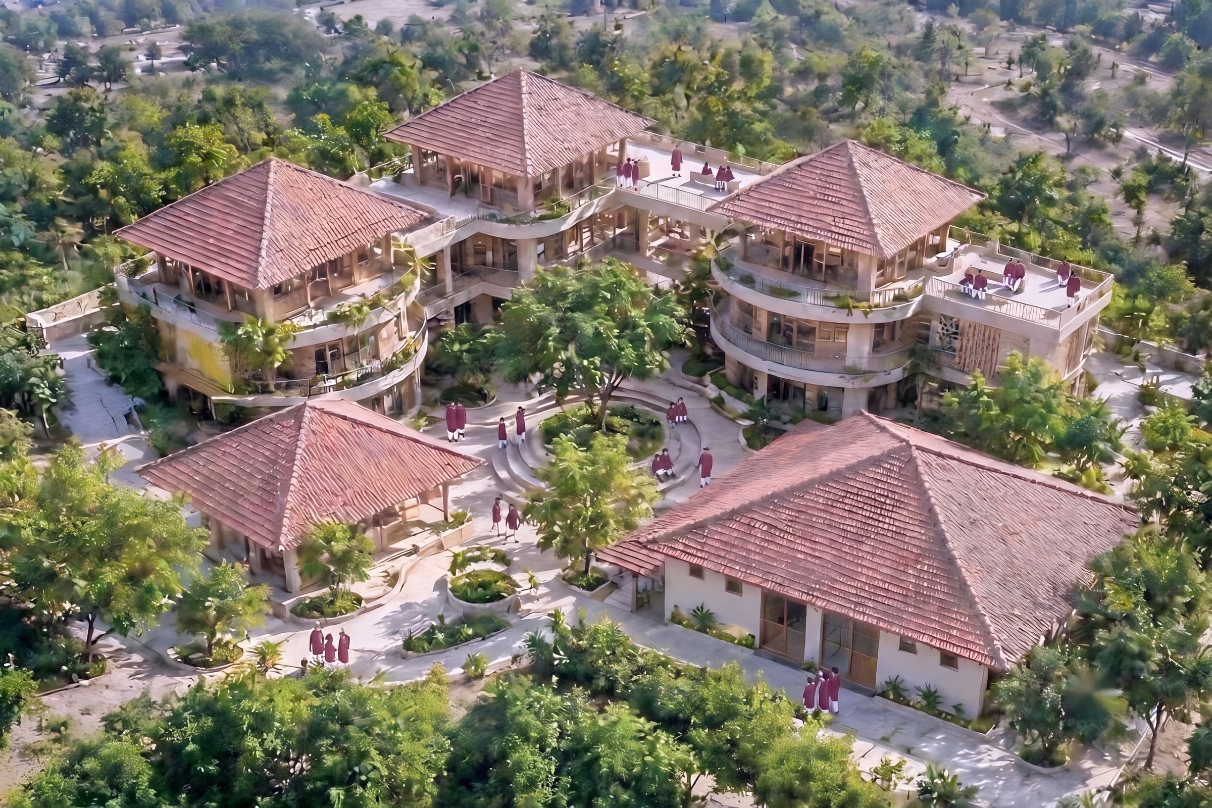 Visualisation from above: four tiled-roof blocks around a courtyard and a big tree, with children in maroon walking the paths