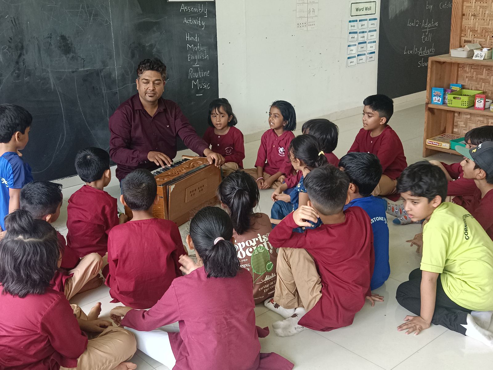 A teacher plays the harmonium for a circle of children on the floor