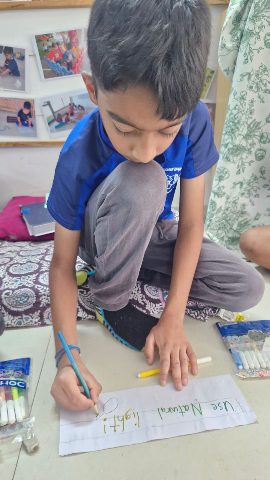 A boy in blue kit kneels to write a “Use natural light” poster