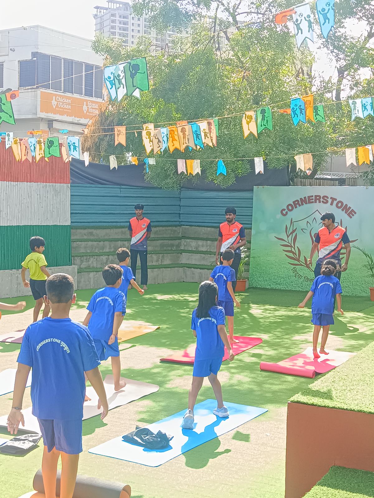 Children in blue sports kit play on the turf under bunting